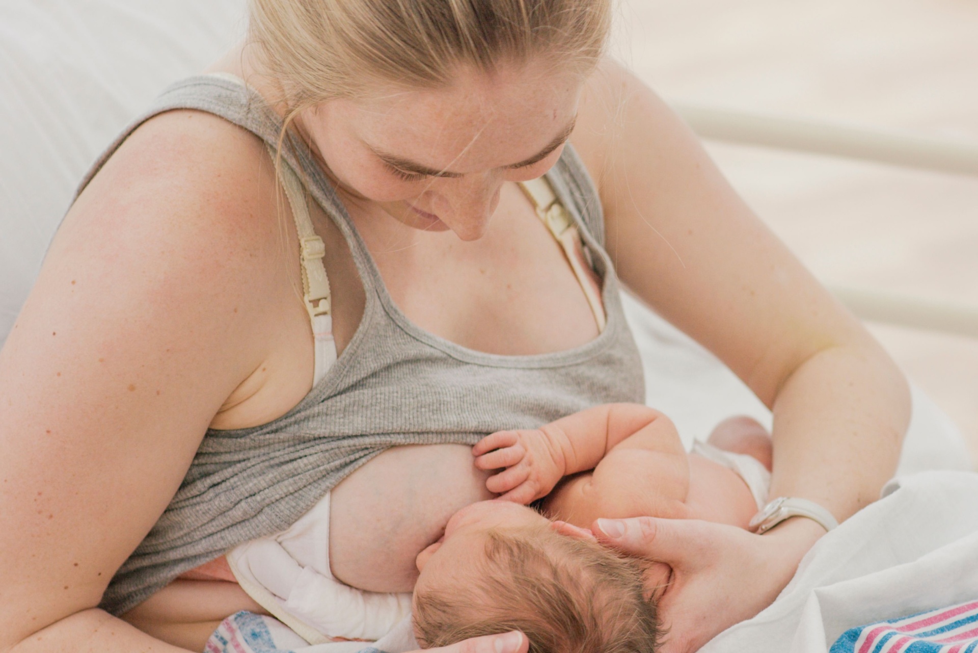 Close-up of a parent's hands cradling a swaddled newborn baby.